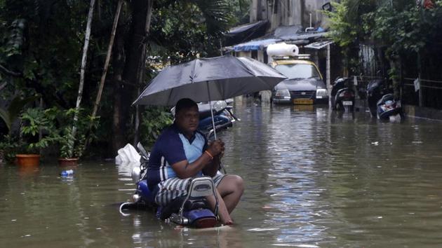 A man sits holding an umbrella on a parked motorcycle at a water logged street after heavy rain in Mumbai, India, Wednesday, Sept. 23, 2020.(AP photo)