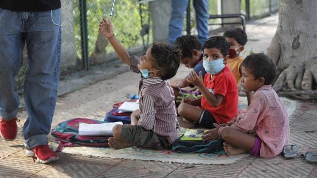 A child takes a pencil during a class conducted by a former diplomat Virendra Gupta and his singer wife Veena Gupta on a sidewalk in New Delhi on Sept. 3, 2020.(AP Photo)