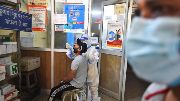 A health worker in PPE coveralls collects a swab sample from a person for coronavirus testing, at a government dispensary in New Delhi.(Raj K Raj/ Hindustan Times)