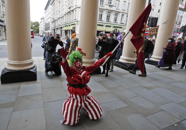 An actor dressed as a pantomime dame kneels in front of a theatre during a march on Parliament to demand more support for the theatre sector amid the COVID-19 pandemic in London, Wednesday, Sept. 30, 2020. (AP)