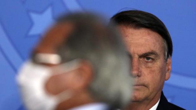 Wearing a mask to curb the spread of the new coronavirus, Brazilian Minister of Economy Paulo Guedes walks past Brazil's President Jair Bolsonaro in Brasilia, Brazil. (AP) Wearing a mask to curb the spread of the new coronavirus, Brazilian Minister of Economy Paulo Guedes walks past Brazil's President Jair Bolsonaro in Brasilia, Brazil. (AP)