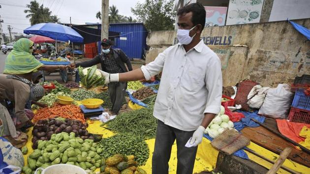 A vegetable vendor wearing gloves and face mask as a precaution against the coronavirus interacts with a customer in Bengaluru. (AP Photo) A vegetable vendor wearing gloves and face mask as a precaution against the coronavirus interacts with a customer in Bengaluru. (AP Photo)