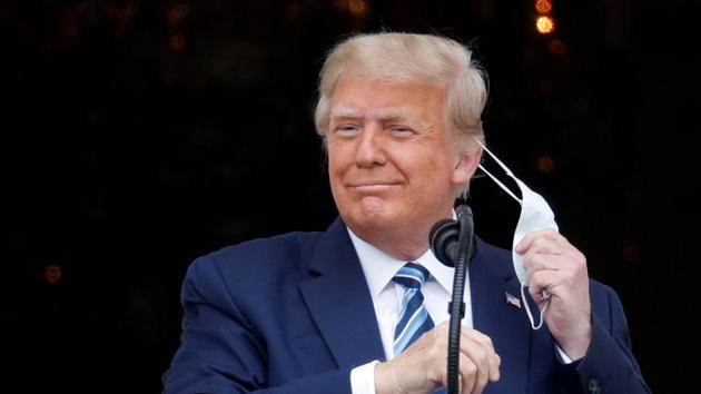 US President Donald Trump, with bandages seen on his hand, takes off his face mask as he comes out on a White House balcony to speak to supporters gathered on the South Lawn for a campaign rally on Saturday.(Reuters)