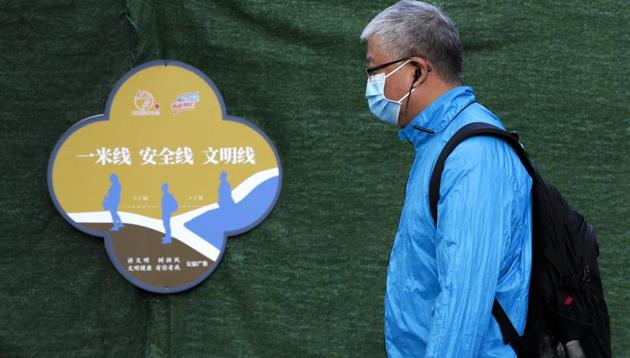 A man wearing a face mask to help curb the spread of the coronavirus walks by a poster which advises people for social distancing, on a street in Beijing (AP Photo/Andy Wong)(AP)