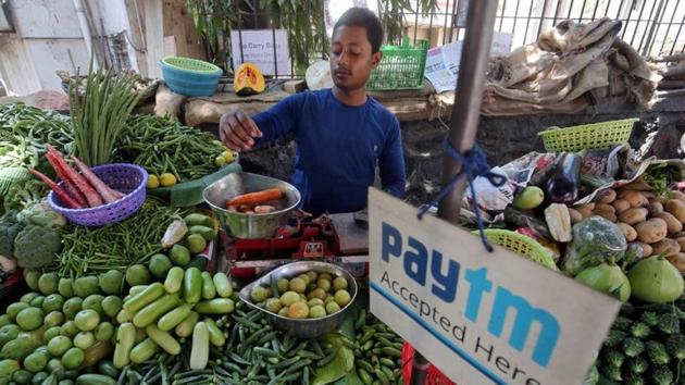 A vendor weighs vegetable next to an advertisement of Paytm, a digital payments firm, hanging amidst his vegetables at a roadside market in Mumbai.(REUTERS)