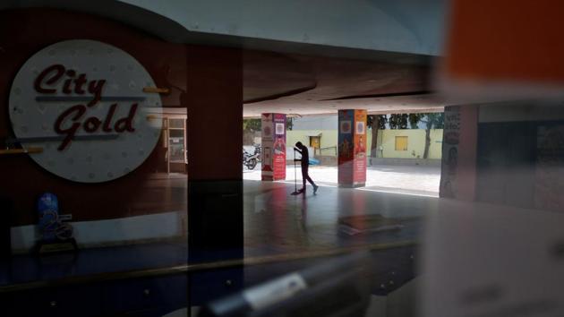 A worker cleans the premises of City Gold cinema after its reopening, amid the outbreak of the coronavirus disease (Covid-19), in Ahmedabad on October 15. People have been advised to use digital modes of payment at theatres. Multiple sale counters for food and beverages will be open, people will be allowed to carry only packed food and no delivery will be permitted inside the auditorium. (Amit Dave / REUTERS)