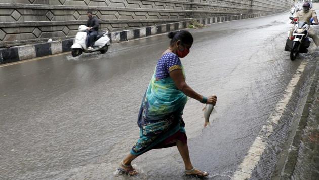 A woman crosses the road with a fish caught in the overflowing rain water near Katraj bridge in Pune on October 15. (Rahul Raut / HT Photo) 