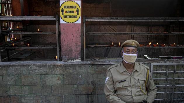 A security person sits wearing a mask outside a temple in Guwahati.(AP) A security person sits wearing a mask outside a temple in Guwahati.(AP)