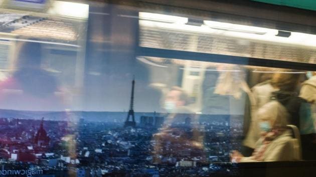 Morning rush hour commuters wear protective face masks while passing a poster showing the Eiffel Tower and city skyline at Champs-Elysees–Clemenceau metro station in Paris, France.(Bloomberg)