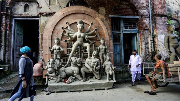 People wearing face masks to prevent the spread of the coronavirus walk past an unfinished clay idol of Hindu deity Durga ahead of the Durga Puja festival in Kolkata on October 17. As the festive week of Navratri kicked off on October 17, devotees are looking forward to celebrating Durga Puja with great enthusiasm. However, the spirit of the auspicious festival has dampened a bit due to the coronavirus pandemic. (Bikas Das / AP)