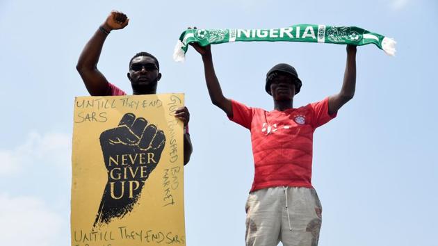 A demonstrator gestures while holding a placard as another holds up a scarf with the colours of the Nigerian national flag during the protest at Magboro, Ogun State on October 20. Authorities imposed the curfew in Lagos on October 20 after the governor, Babajide Sanwo-Olu, said the protests had turned violent. (Pius Utomi Ekpei / AFP)