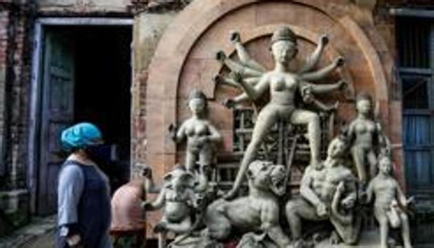 People wearing face masks to prevent the spread of the coronavirus walk past an unfinished clay idol of Hindu goddess Durga ahead of Durga Puja festival in Kolkata. (AP) People wearing face masks to prevent the spread of the coronavirus walk past an unfinished clay idol of Hindu goddess Durga ahead of Durga Puja festival in Kolkata. (AP)