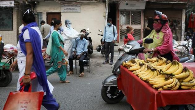 Commuters walk past a health worker collecting swab samples for Covid-19 test at a weekly market in New Delhi on October 13. An average positivity rate of 6.2% was recorded in the last seven days as compared to 5.5% the week before. During the last seven days, 3,269 new cases were reported each day on average as compared to 2,777 cases the week before, HT reported. (Anushree Fadnavis / REUTERS)