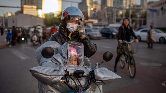 A woman with her daughter in a protective enclosure, wait to cross the road as they ride on an electric bike in Beijing, China on October 21. In contrast to South Asia, countries further east like China and New Zealand have crushed infections and others like Japan, have seen the coronavirus stubbornly entrenched if not accelerating. (Nicolas Asfouri / AFP)