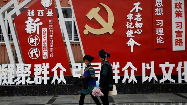 Ethnic Yi women walk past an installation featuring a logo of Communist Party of China at the Chengbei Ganen Community.(REUTERS)