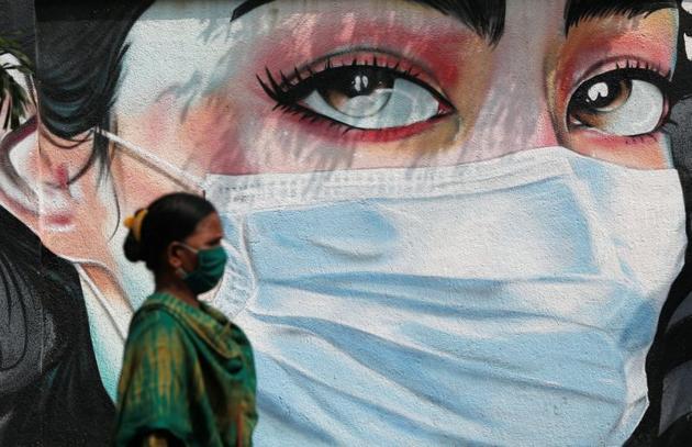 A woman walks past a graffiti of a girl wearing a protective mask amidst the spread of the coronavirus disease in Mumbai, India.(REUTERS)
