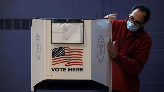 A man disinfects a privacy booth at a polling station in Our Lady Help of Christians, Staten Island, New York City on October 25. The Election Project has predicted that turnout this year could top 150 million in total. Some 137 million ballots were cast in the 2016 election. (Andrew Kelly / REUTERS)