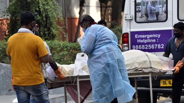 A relative wearing Personal Protective Equipment (PPE) near a handcart carrying the body of a person who died from the Covid-19, at Nigambodh Ghat cremation ground, in New Delhi.(Sanjeev Verma/HT PHOTO) A relative wearing Personal Protective Equipment (PPE) near a handcart carrying the body of a person who died from the Covid-19, at Nigambodh Ghat cremation ground, in New Delhi.(Sanjeev Verma/HT PHOTO)