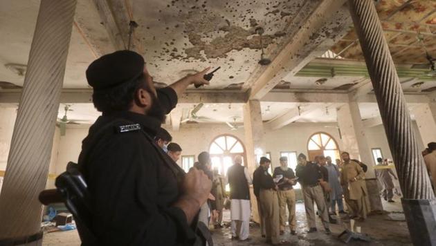 A police officer points to the damaged roof while others survey the site of a bomb blast at a religious seminary in Peshawar, Pakistan on October 27.(Reuters)