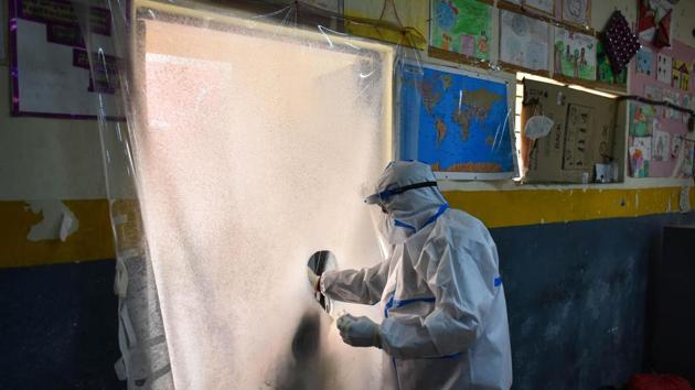 A health worker in PPE coveralls collects a swab sample from behind a protective screen for coronavirus testing, at Khajuri Khas in New Delhi (Photo by Sanchit Khanna/ Hindustan Times)