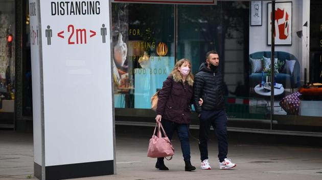 Shoppers with masks on walks past stores and a sign urging people to keep a 2-metre social distance from each other in London on November 1. The new restrictions apply across England, with the other three devolved nations of Scotland, Wales and Northern Ireland already under varying degrees of complete lockdowns. (Justin Tallis / AFP)