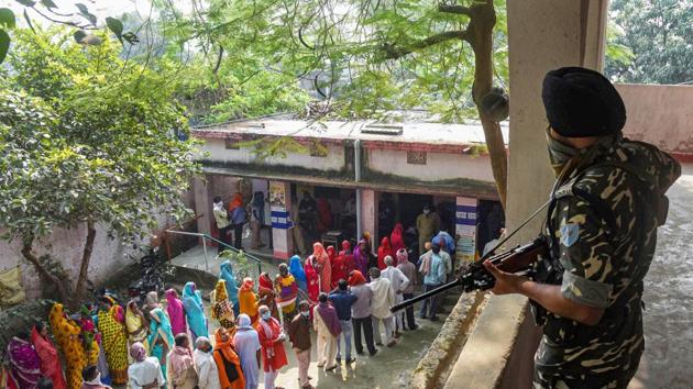 A security official keeps a vigil as voters stand in queues to cast their votes at a polling station during the third phase of Bihar Assembly Elections, at Mahua in Vaishali district.(PTI)