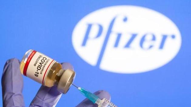 A woman holds a small bottle labeled with a " Covid-19 Vaccine" sticker and a medical syringe in front of displayed Pfizer logo in this illustration.(REUTERS)