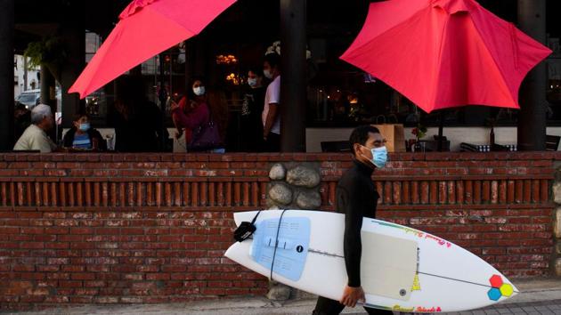 A surfer walks past outdoor diners in Manhattan Beach, California on November 21, a few hours before the start of a new 10pm to 5am curfew during increased Covid-19 restrictions. With coronavirus cases in the United States now exceeding 12 million, the virus continues its resurgence throughout the country, prompting governors of various states to issue a patchwork of area-specific restrictions. (Patrick T. Fallon / AFP) A surfer walks past outdoor diners in Manhattan Beach, California on November 21, a few hours before the start of a new 10pm to 5am curfew during increased Covid-19 restrictions. With coronavirus cases in the United States now exceeding 12 million, the virus continues its resurgence throughout the country, prompting governors of various states to issue a patchwork of area-specific restrictions. (Patrick T. Fallon / AFP)