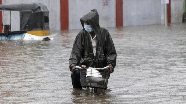 A man wearing a mask as a precaution against the coronavirus pedals his cycle through a flooded street in Chennai on November 25. Cyclonic winds brought nearly 237 mm of rainfall to Puducherry until 2.30am on November 25. Cuddalore recorded 246 mm rainfall, while Chennai and Karaikal received 89 mm rainfall due to the storm. (R. Parthibhan / AP) 