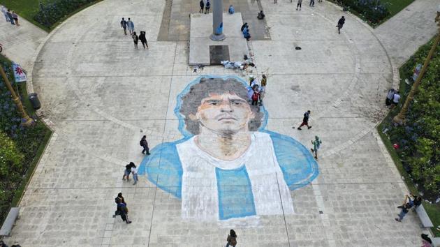 People walk past a mural of Maradona painted on the Plaza de Mayo in front of the presidential palace in Buenos Aires, Argentina on November 26. (Rodrigo Abd / AP)