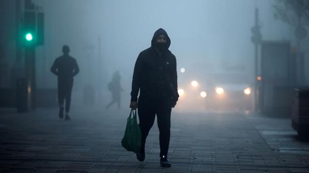 Pedestrians, some wearing a face mask walk in the early morning fog in Walthamstow, east London on November 27.(AFP)