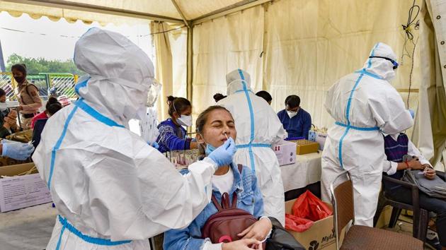 A health worker, wearing protective gear, collects swab sample of a passenger at Anand Vihar ISBT in New Delhi.(PTI)