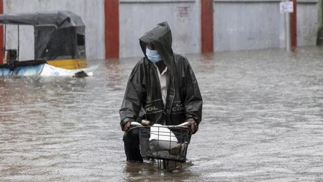 A man wearing a mask as a precaution against Covid-19 pedals his cycle through a flooded street in Chennai last week.(AP Photo)