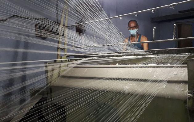 A worker wearing a protective face mask works on a loom in a textile factory amidst the coronavirus disease (Covid-19) outbreak. (Reuters)