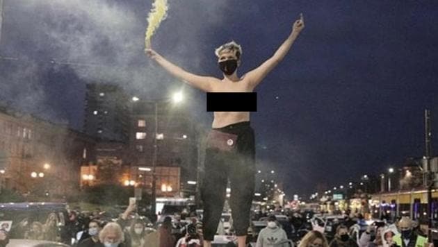 Karolina Micula stripped to her waist and stood on top of a car at a busy Warsaw intersection during a protest, holding a flare high and giving the middle finger.(Instagram) Karolina Micula stripped to her waist and stood on top of a car at a busy Warsaw intersection during a protest, holding a flare high and giving the middle finger.(Instagram)