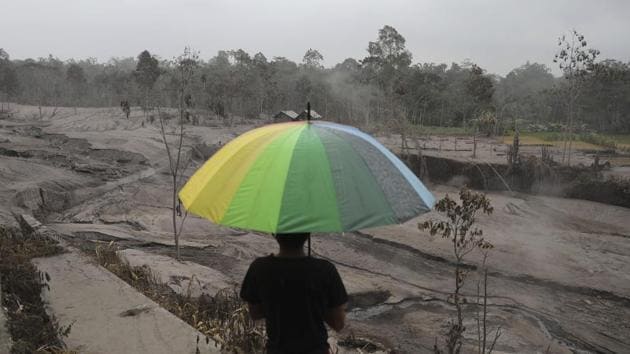 A man holds an umbrella as he looks at the damages caused by the eruption of Mount Semeru, in Lumajang, East Java, Indonesia on December 3. (Trisnadi / AP)