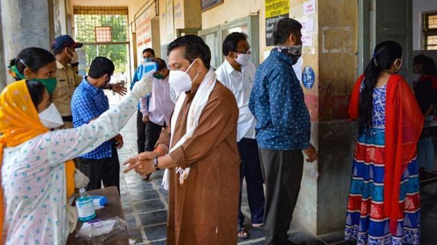 A health worker checks the temperature of a voter as others wait in queues to cast their votes during the graduates’ and teachers' constituency polls for Maharashtra legislative council, in Karad on December 1.(File photo) A health worker checks the temperature of a voter as others wait in queues to cast their votes during the graduates’ and teachers' constituency polls for Maharashtra legislative council, in Karad on December 1.(File photo)