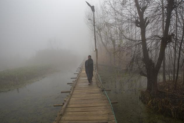 A Kashmiri man shields his face from cold as he walks over a foot bridge through dense fog on a cold morning on the outskirts of Srinagar on Thursday.(AP)