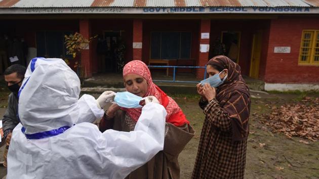 A health worker hands out face masks to voters during District Development Council (DDC) elections, in Ganderbal, Jammu and Kashmir on December 10. India recorded 30,254 new cases of the coronavirus disease (Covid-19) between December 12 and 13 morning, which pushed the nationwide tally up to 98,57,029, according to Union health ministry’s update. (Waseem Andrabi / HT Photo)