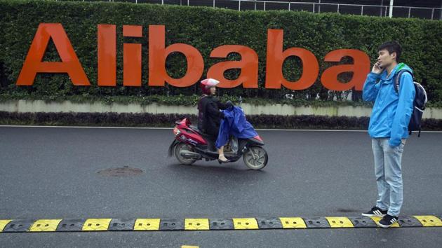 In this file photo, a man talks on his phone as a woman rides on an electric bike past a company logo at the Alibaba Group headquarters in Hangzhou in eastern China's Zhejiang province. China’s market regulator on Monday, Dec. 14, 2020 said it fined Alibaba Group and a Tencent Holdings-backed company for failing to seek approval before proceeding with some acquisitions. (AP Photo/Ng Han Guan, File) In this file photo, a man talks on his phone as a woman rides on an electric bike past a company logo at the Alibaba Group headquarters in Hangzhou in eastern China's Zhejiang province. China’s market regulator on Monday, Dec. 14, 2020 said it fined Alibaba Group and a Tencent Holdings-backed company for failing to seek approval before proceeding with some acquisitions. (AP Photo/Ng Han Guan, File)