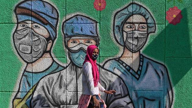 A woman walks past a mural representing a frontline warrior of the Covid-19 coronavirus, painted on a wall along the roadside in New Delhi on December 19. According to the World Health Organization, if the positivity rate remains 5% or below for two weeks, a region can be said to be keeping its outbreak under control and is testing adequately. India’s positivity rate has been below this threshold for 25 days now, HT reported. (Sajjad Hussain / AFP) 