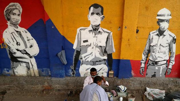 A roadside barber cuts the hair of a man in front of a wall with graffiti, amidst the spread of the coronavirus disease (Covid-19), in Mumbai, India.(REUTERS)