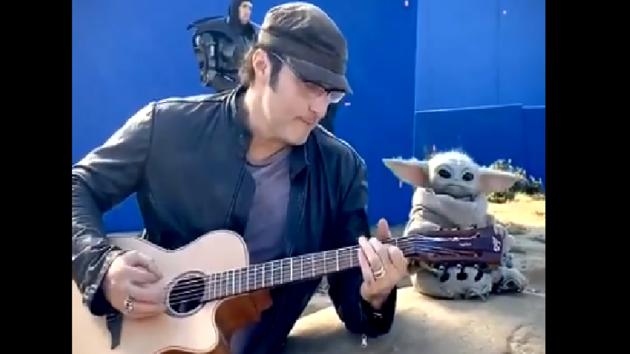 The image shows director Robert Rodriguez playing the guitar as Baby Yoda sits beside him.(Twitter/@Rodriguez)