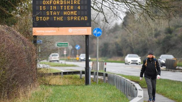 A person walks past a roadside public health information sign near Oxford on December 28. In response, authorities have put a swath of England that’s home to 24 million people under restrictions that require non-essential shops to close, bar indoor socializing and allow restaurants and pubs only to operate for takeout. (Toby Melville / REUTERS) 