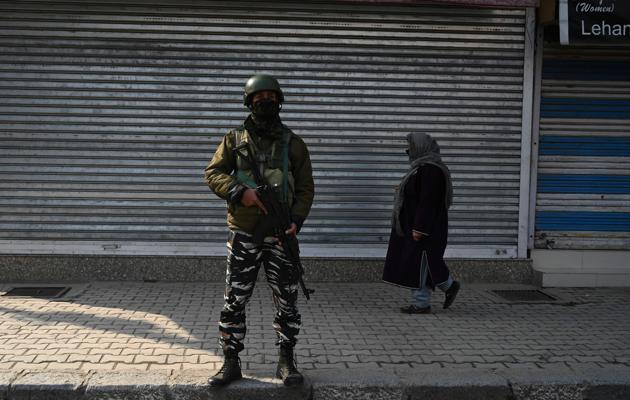 A woman walks past a securityman standing guard in front of closed shops in Srinagar on January 1.(AFP)