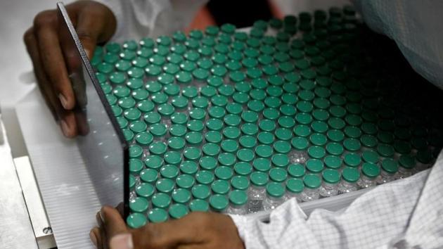 An employee in personal protective equipment removes vials of SII's Covishield from a visual inspection machine.(REUTERS)