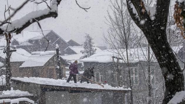 Men clear snow from the roof of their workshop as it snows in Pulwama, south of Srinagar, Kashmir, Monday.(AP)