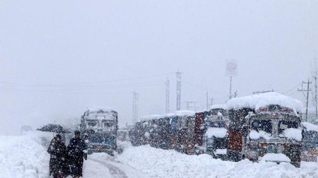 People walk past stranded vehicles on the Jammu-Srinagar National Highway during heavy snowfall, at Qazigund in Anantnag district of South Kashmir on January 5.(PTI)