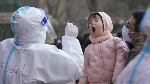 A medical staff in a protective suit prepares to take a swab from a child near a residential area in Shijiazhuang in north China's Hebei province.(AP) A medical staff in a protective suit prepares to take a swab from a child near a residential area in Shijiazhuang in north China's Hebei province.(AP)
