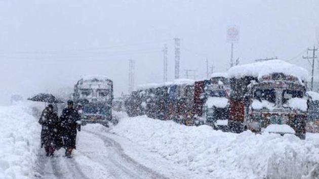 People walk past stranded vehicles on the Jammu-Srinagar National Highway during heavy snowfall at Qazigund in Anantnag district of South Kashmir earlier this week.(PTI PHOTO.)